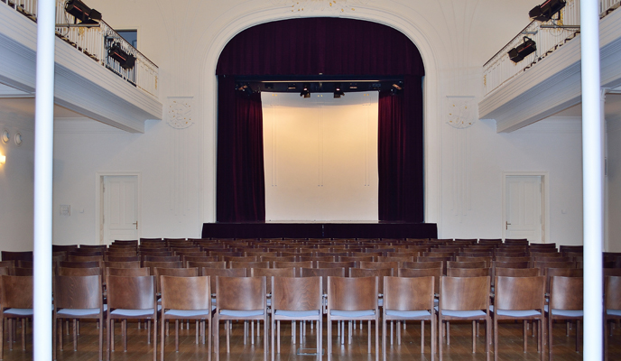 Jugenstilsaal mit Bestuhlung und Blick zur Bühne mit roten Samtvorhang